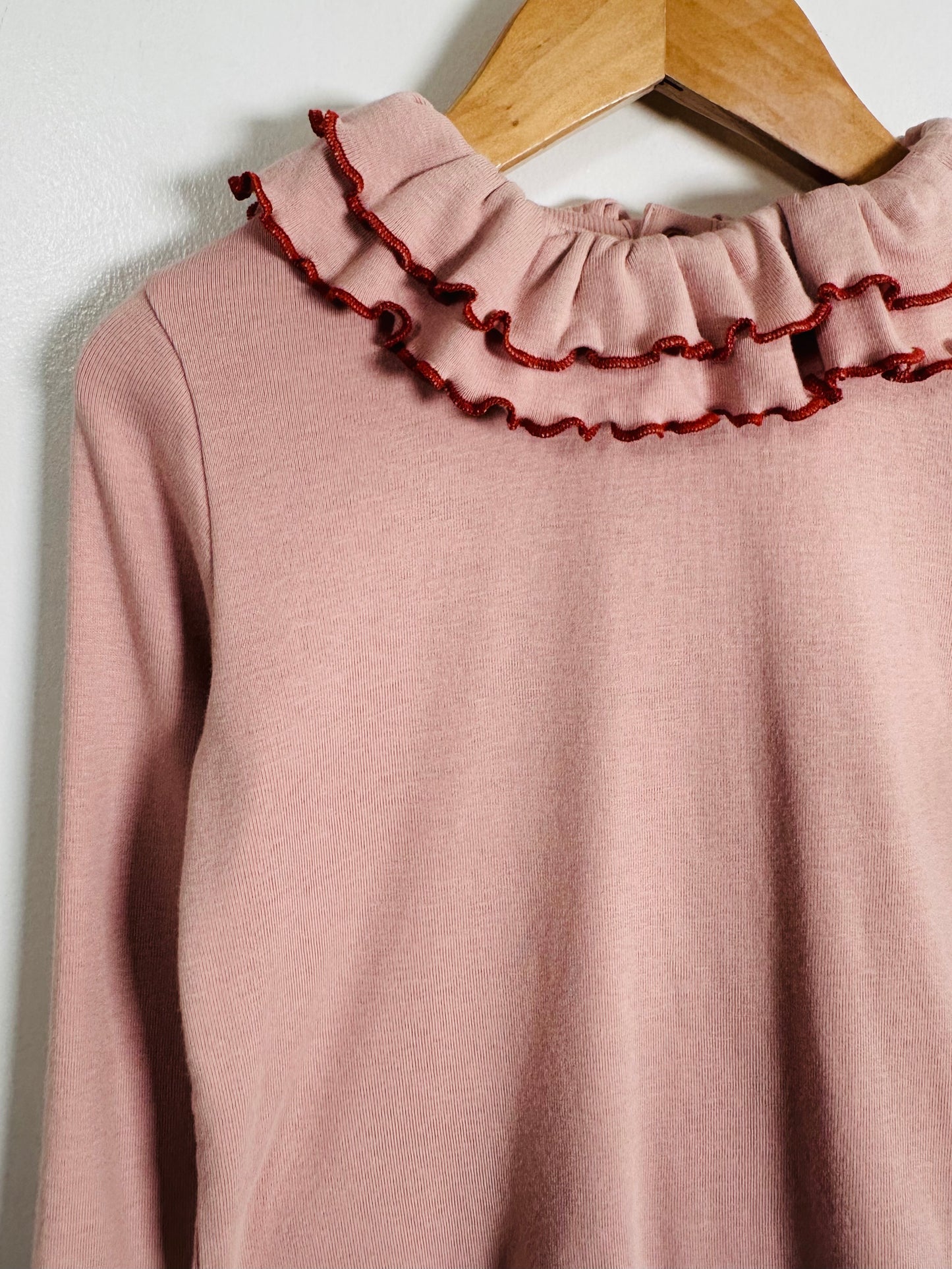 Pink sweater with ruffled collar on a wooden hanger against a white background
