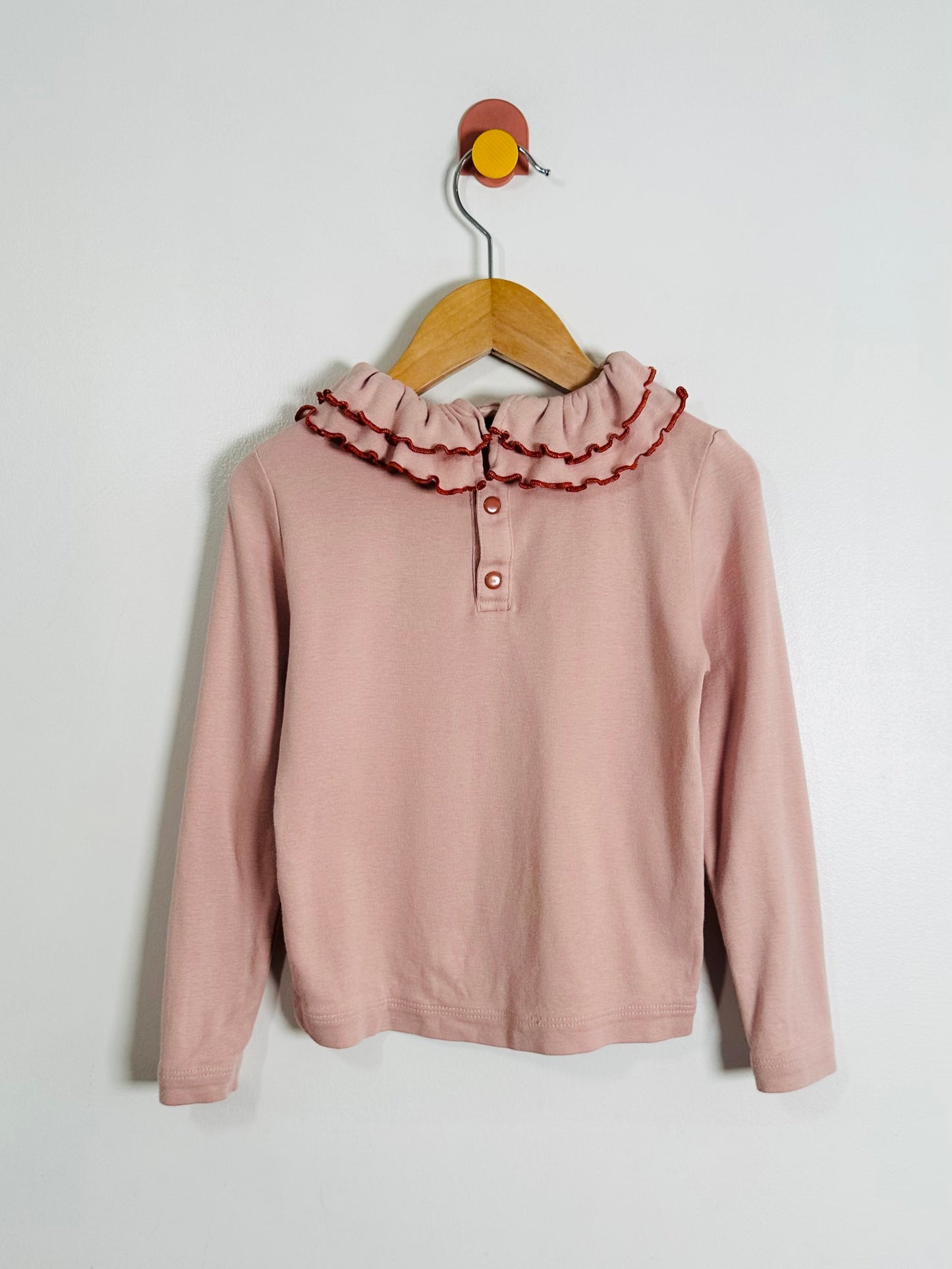 Pink blouse with ruffled collar on a wooden hanger against a white background
