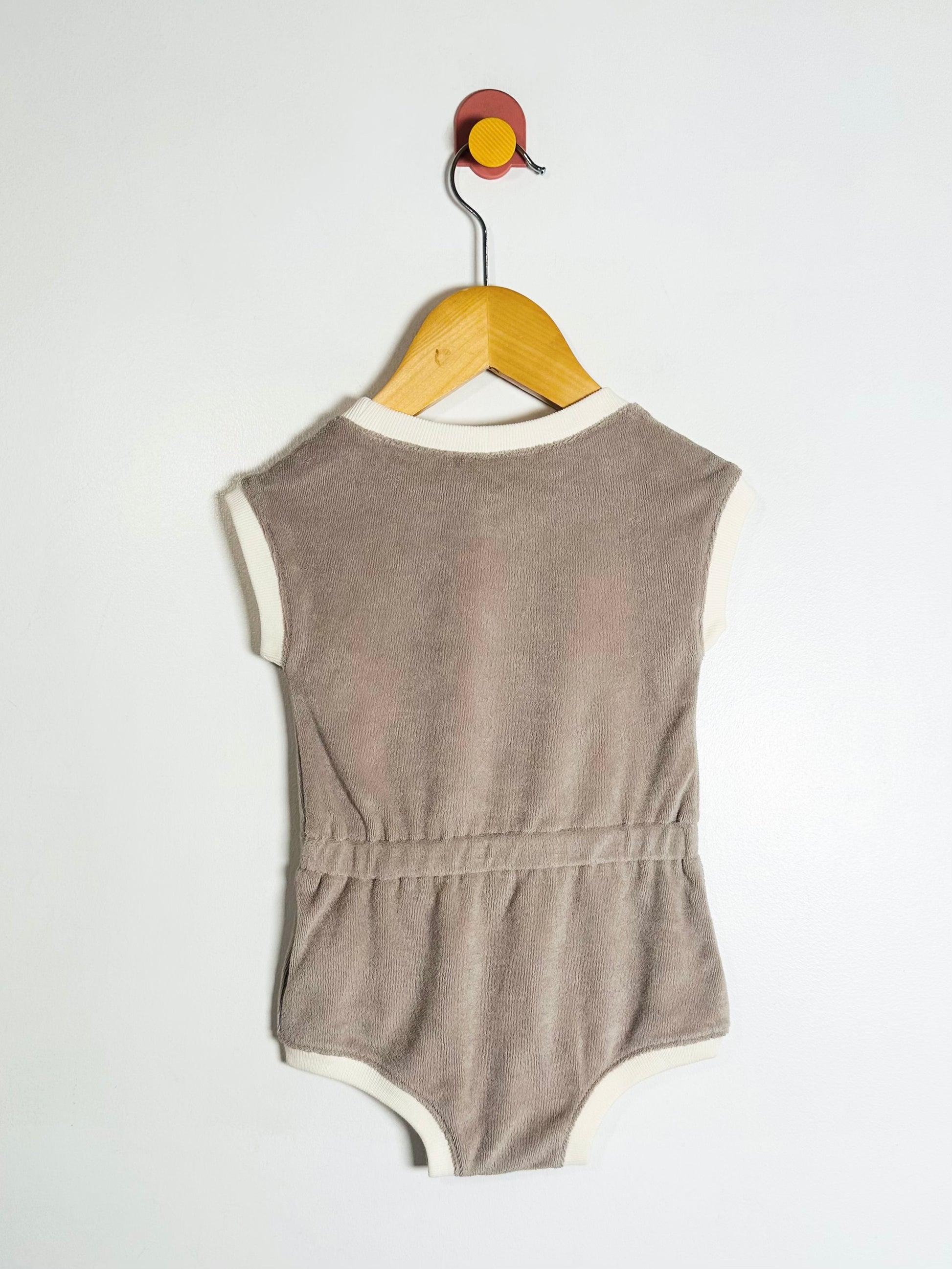 Brown baby romper on a wooden hanger against a white background