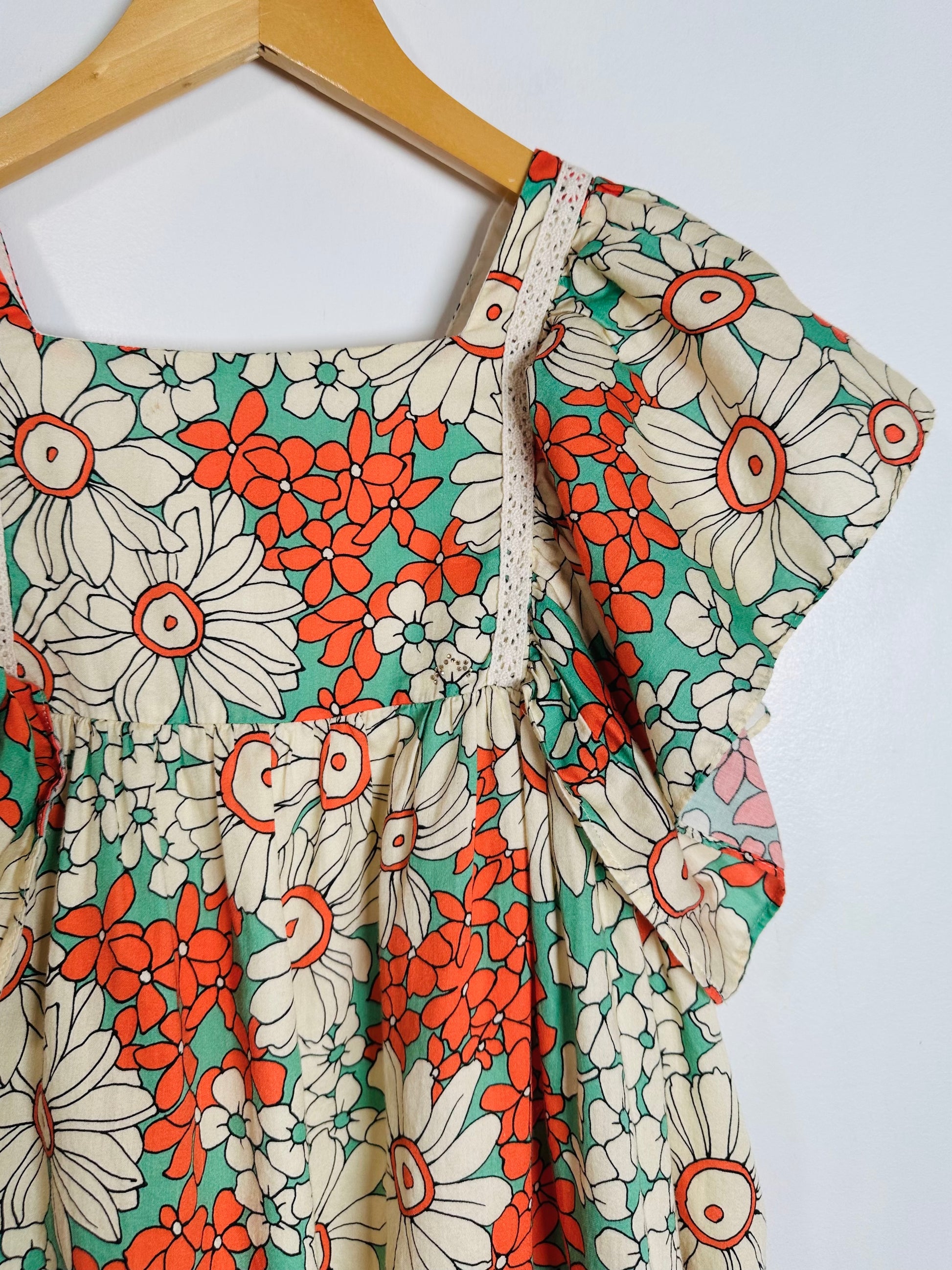 Floral dress with orange and green pattern on a wooden hanger