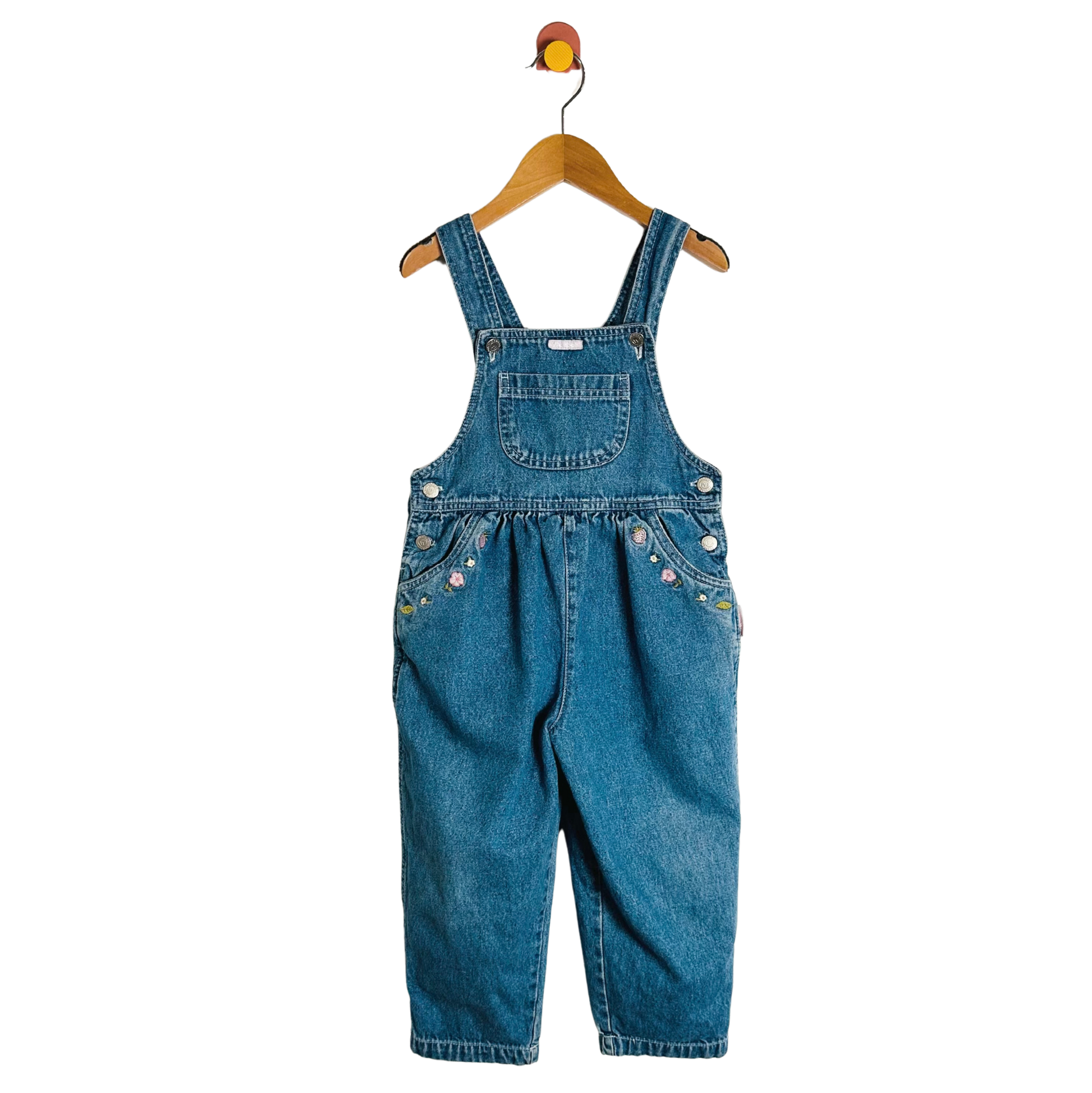 Blue denim overalls on a wooden hanger against a white background