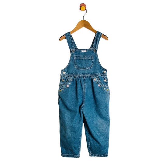 Blue denim overalls on a wooden hanger against a white background