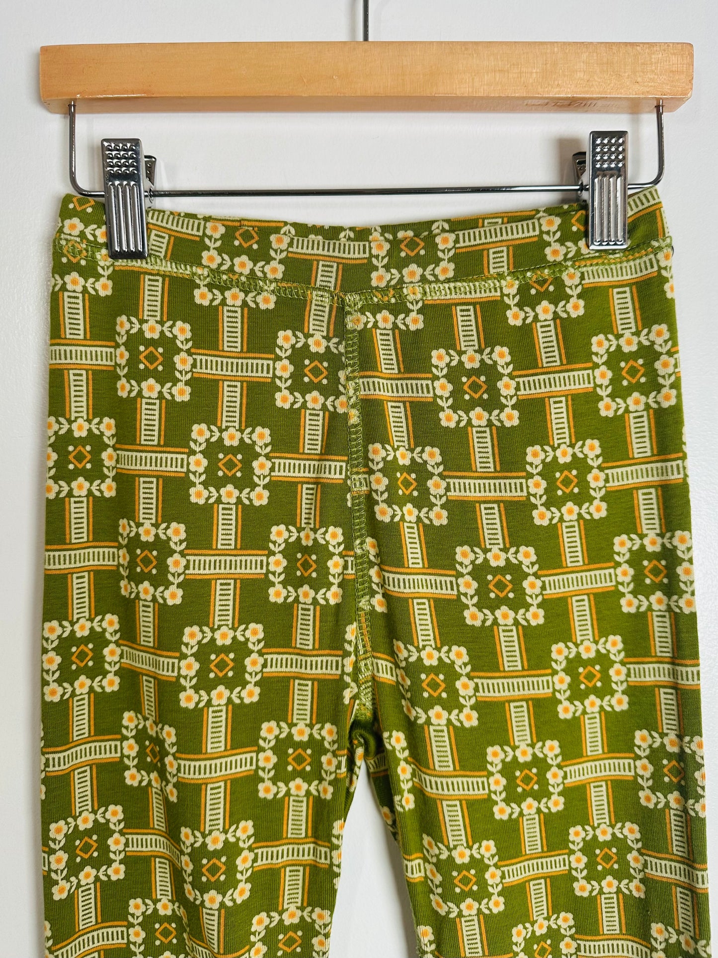 Green patterned pants hanging on a wooden hanger against a white background