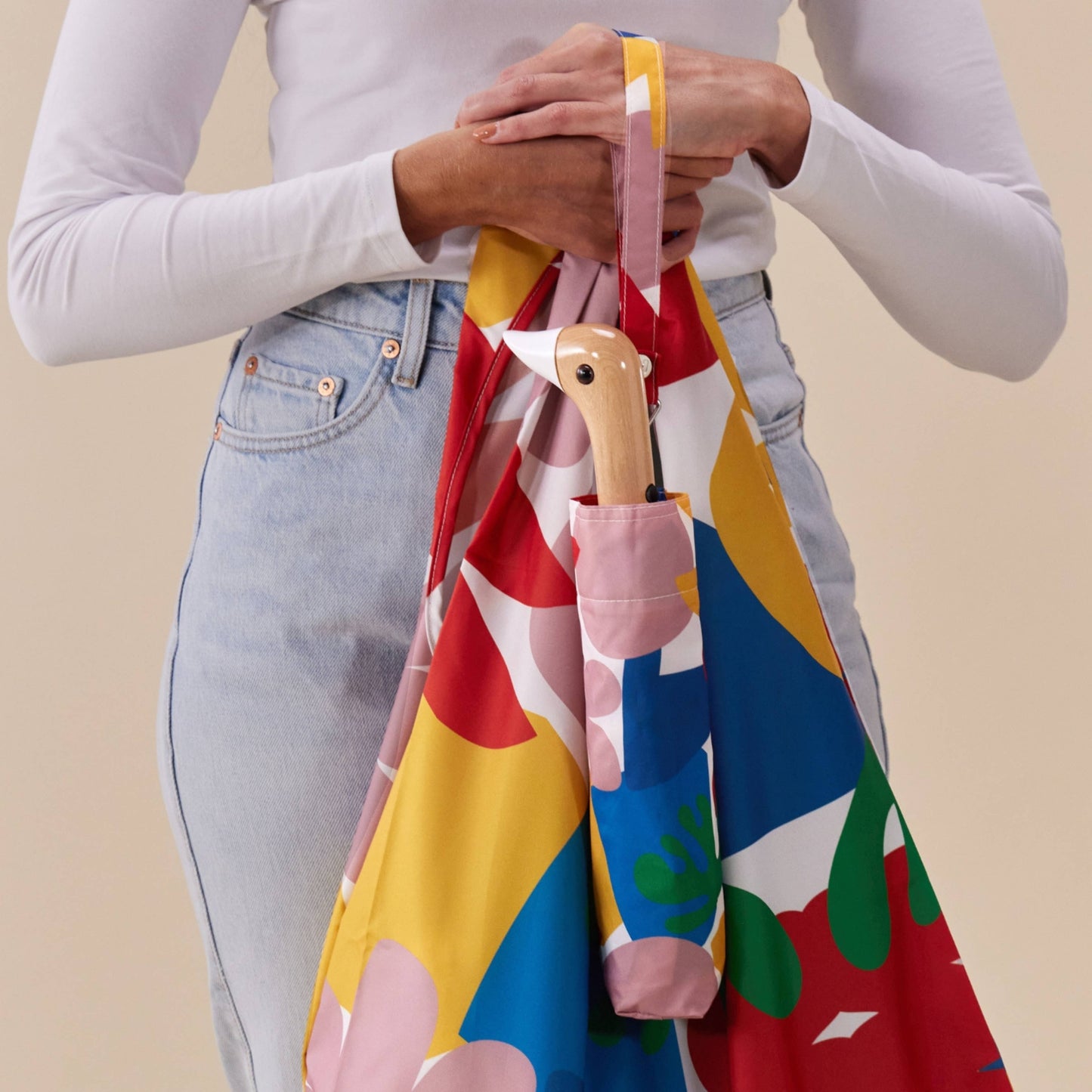 Person holding a colorful bag with a patterned handle against a beige background