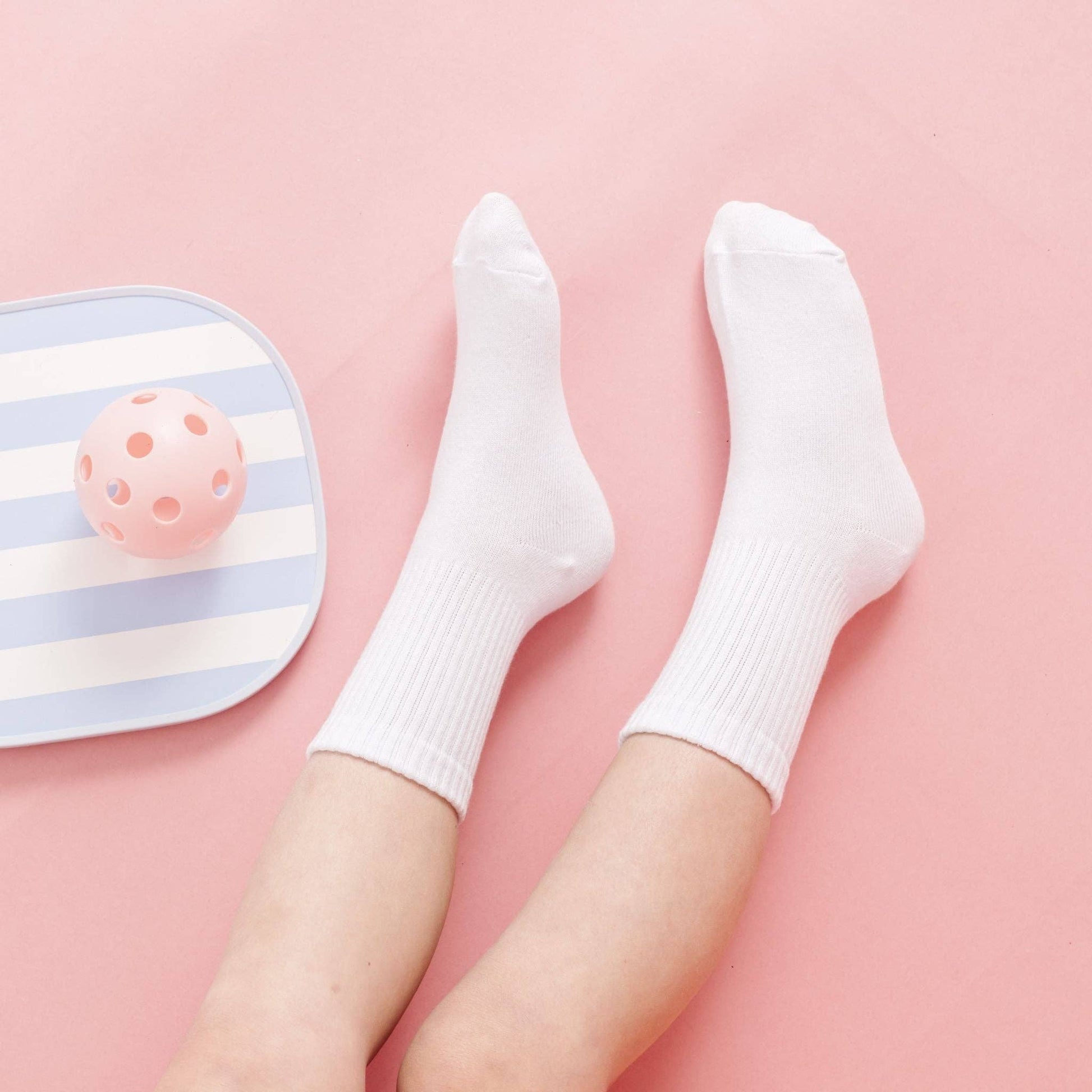 White socks on a pink background with a striped foot massager.