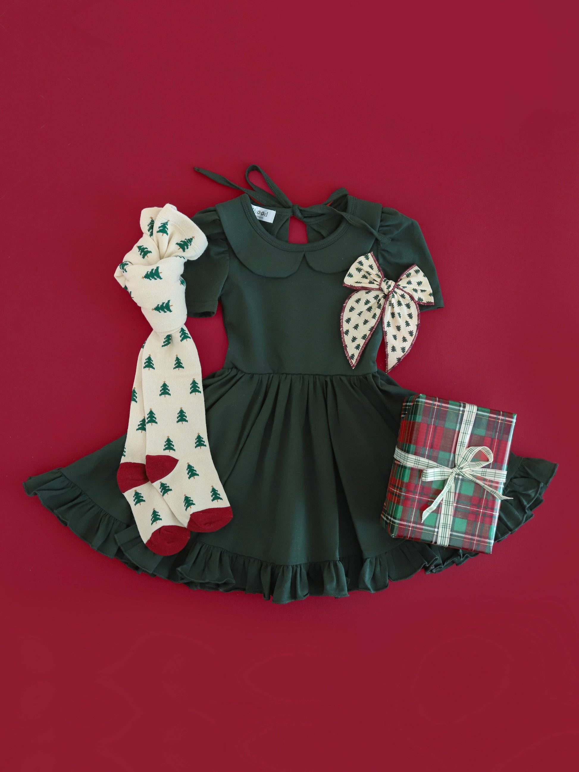 Children's outfit with green dress, patterned bow, and Christmas-themed socks on a red background