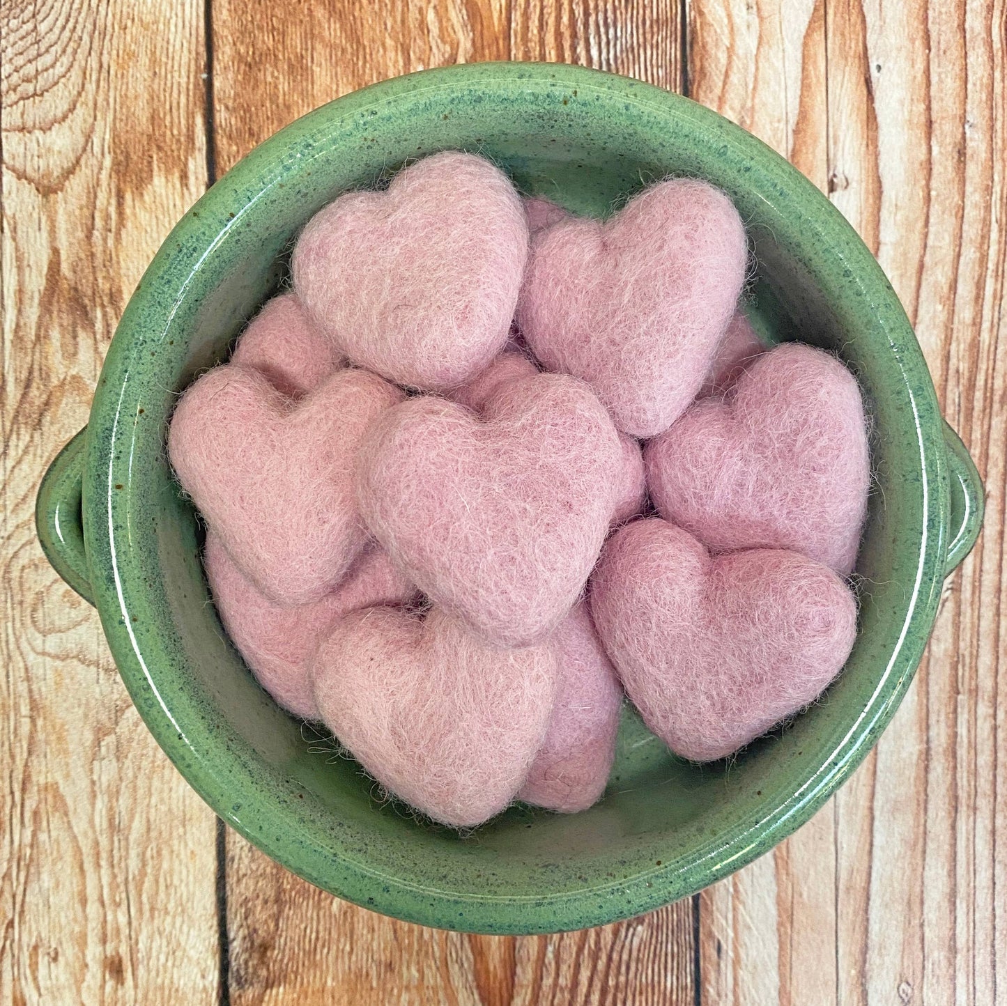 Pink heart-shaped objects in a green bowl on a wooden surface