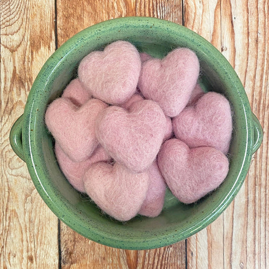 Pink heart-shaped objects in a green bowl on a wooden surface