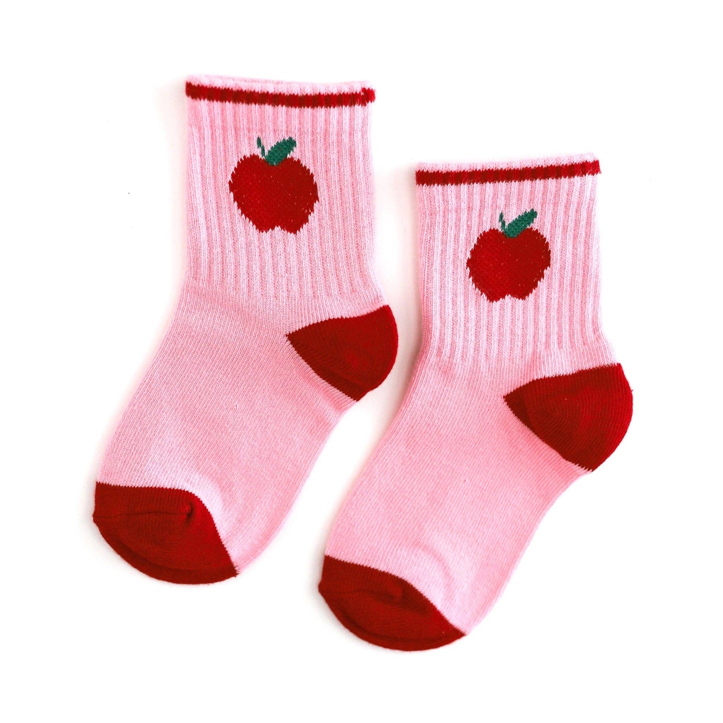 A pair of light pink ribbed ankle socks with red toe and heel sections, featuring a red apple with a green stem knitted onto the upper leg, shown on a plain white background.
