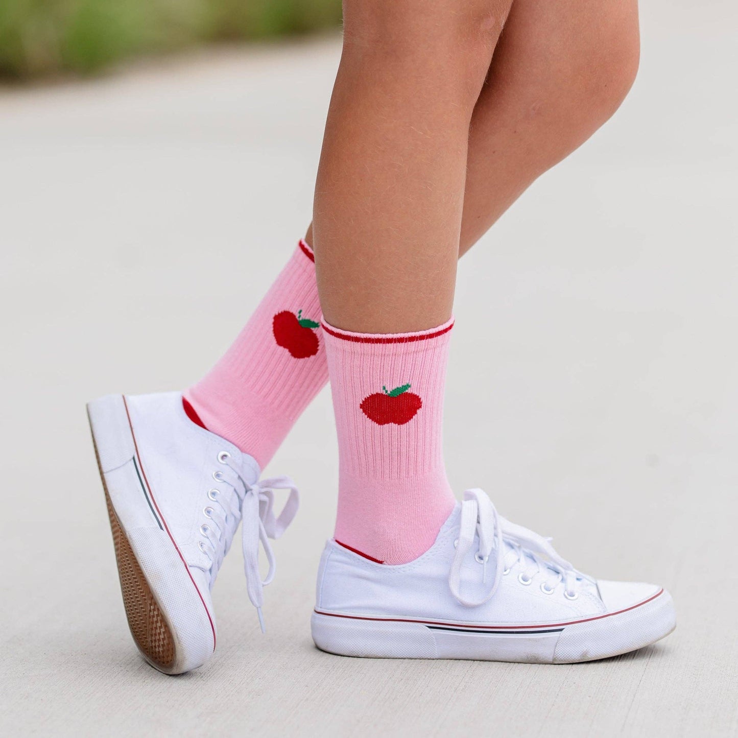 Pink socks with red apple design worn with white sneakers on a light background