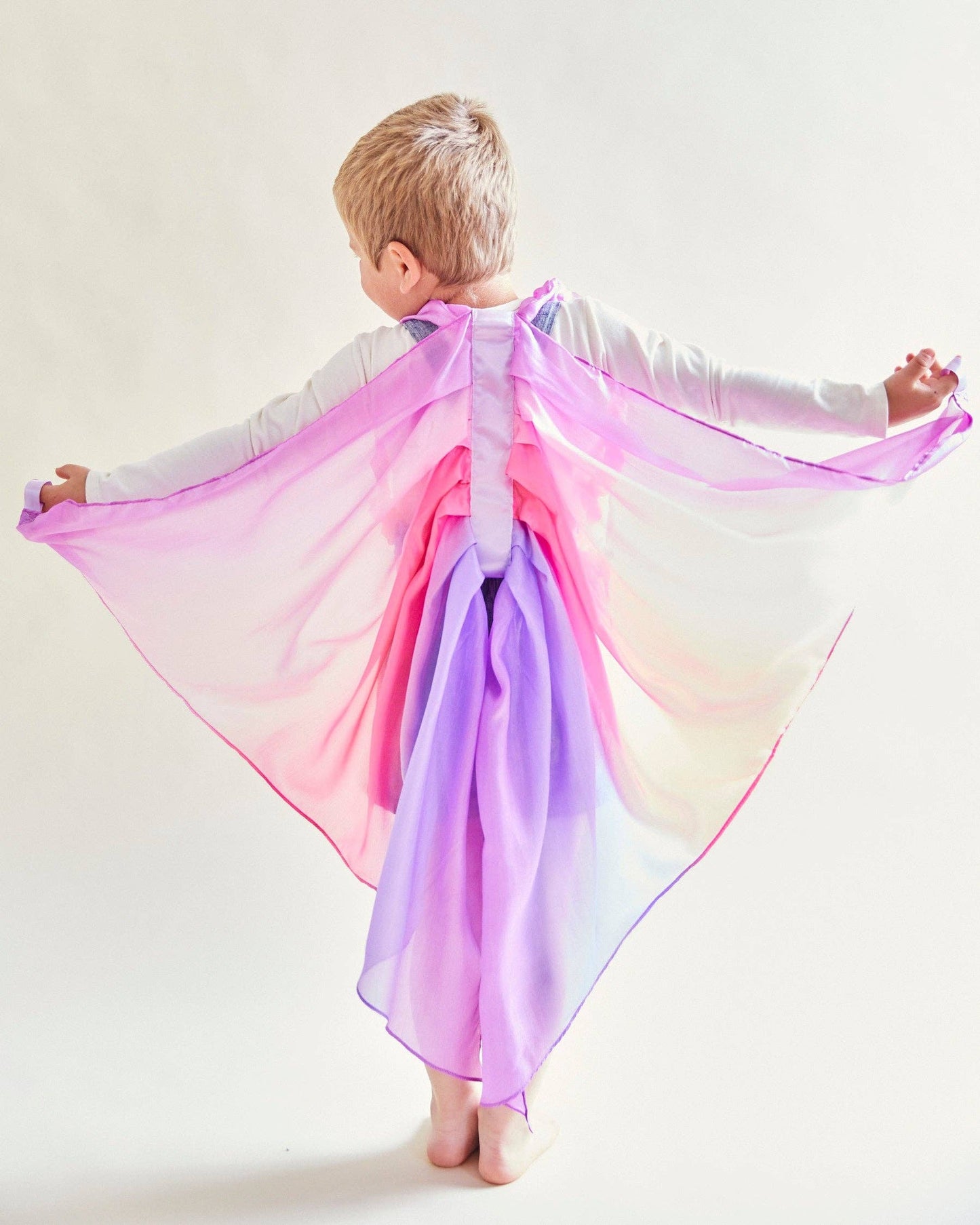 Child wearing a colorful cape with a gradient from pink to purple on a white background