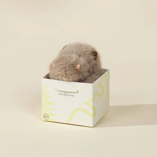 Small fluffy animal in a white box with yellow text on a beige background
