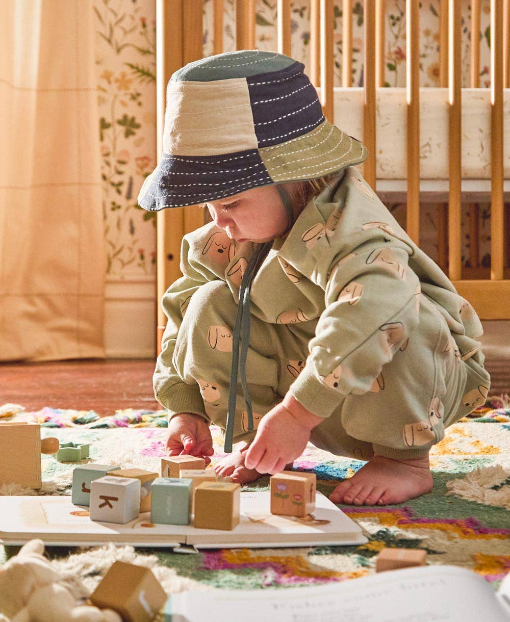 Child playing with wooden blocks on a colorful rug in a home setting.