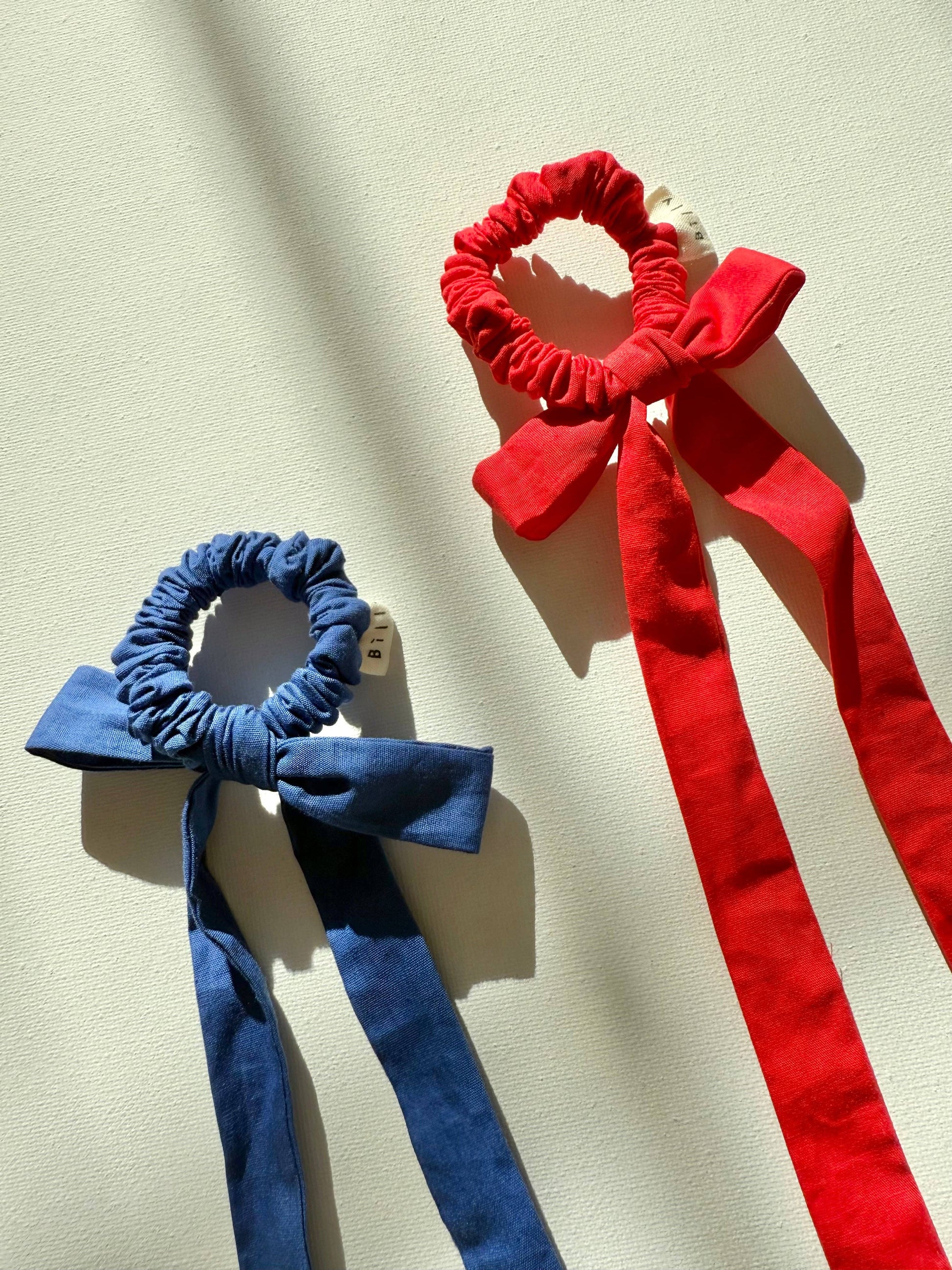 Red and blue scrunchies with decorative bows on a beige background