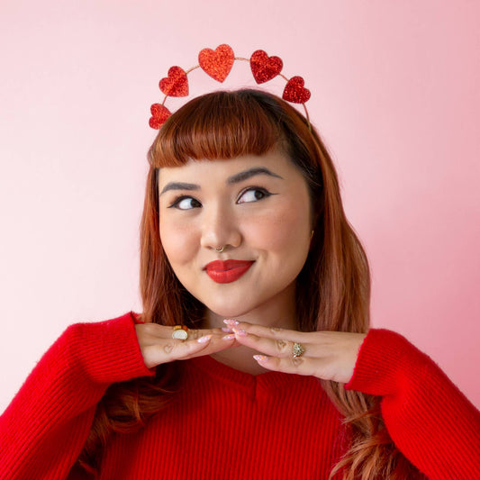 Woman wearing a red heart headband against a pink background