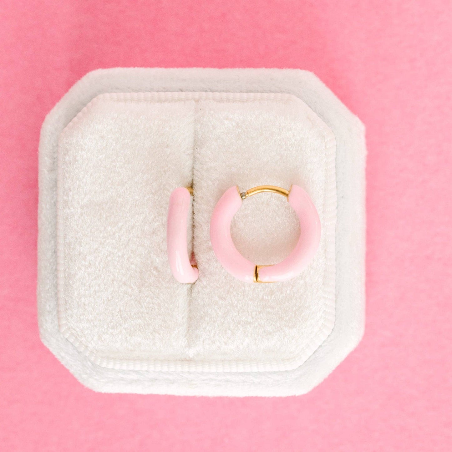 Pink hoop earrings in a white jewelry box on a pink background