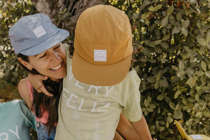 Two people wearing bucket hats with visible brand logos against a green leafy background.