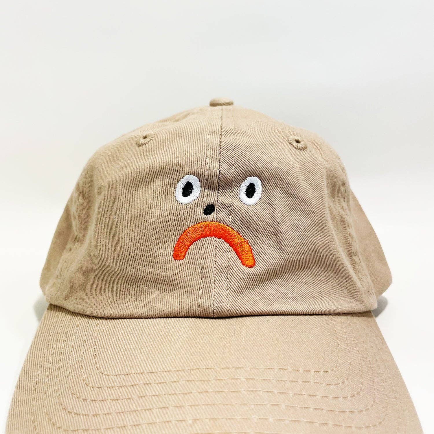 Beige cap with a sad face design on a white background