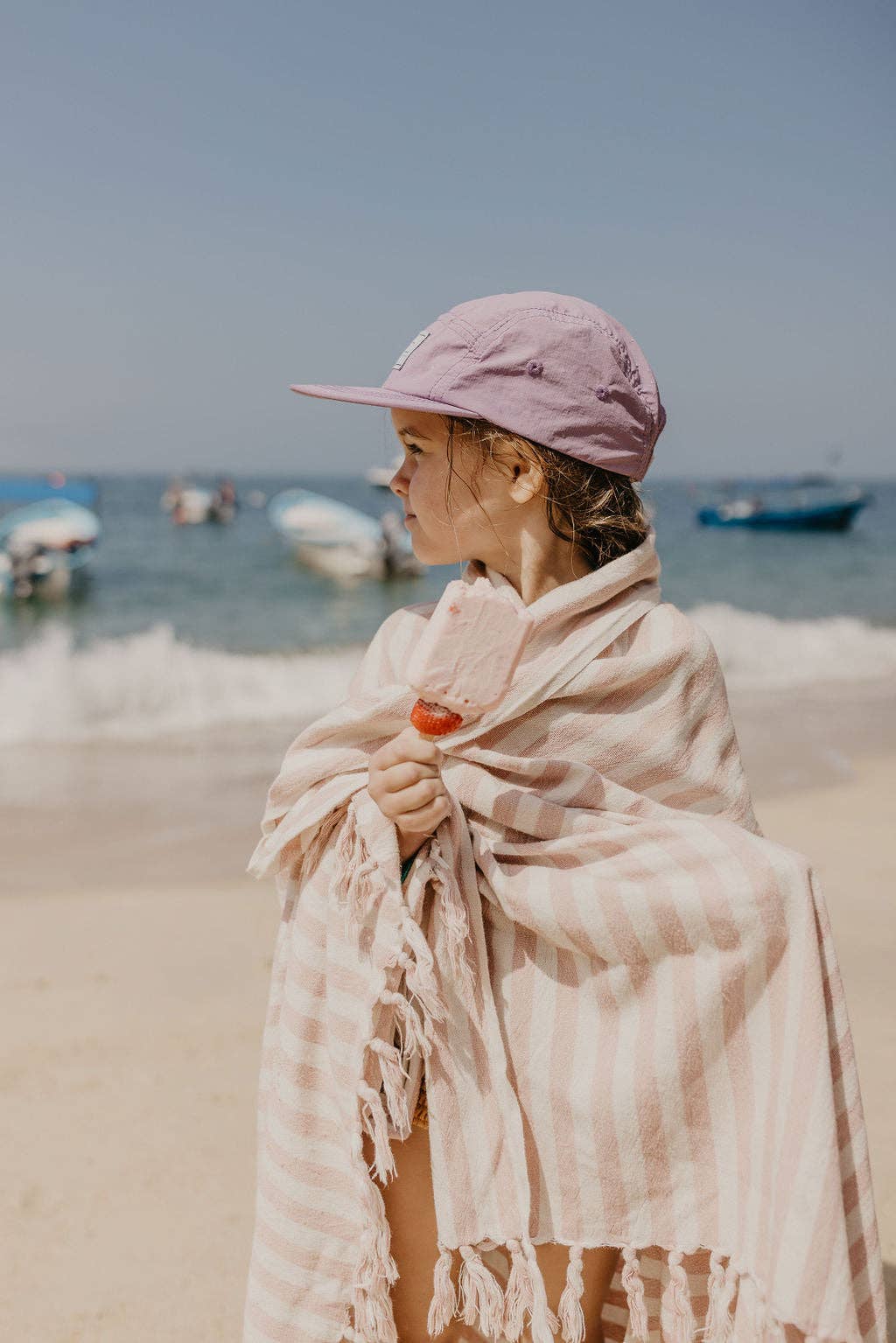Person wrapped in a towel on a beach with boats in the background
