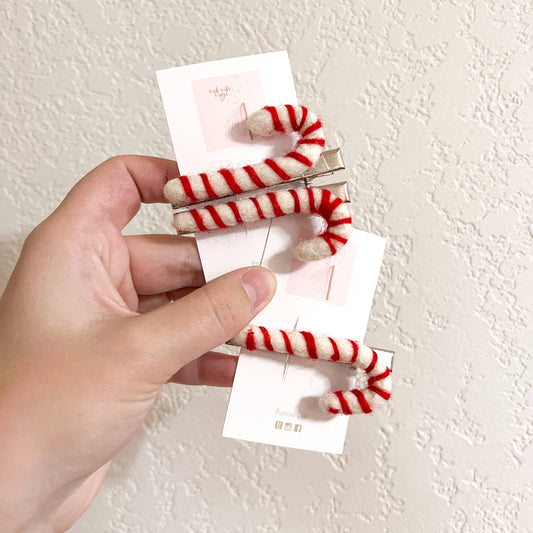 Hand holding a set of red and white striped hair clips against a light background
