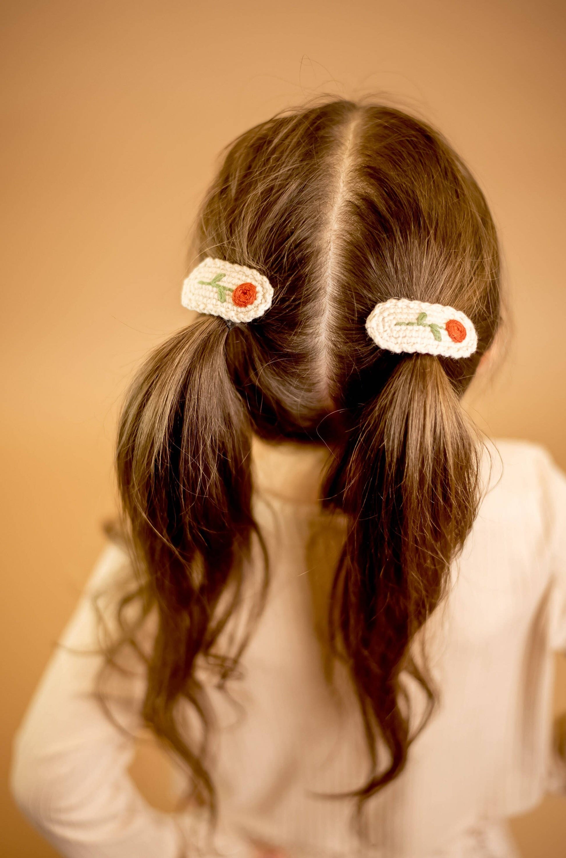 Person with pigtails wearing floral hair clips against a beige background