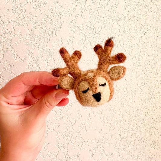 Hand holding a small felt reindeer hair against a textured beige wall.