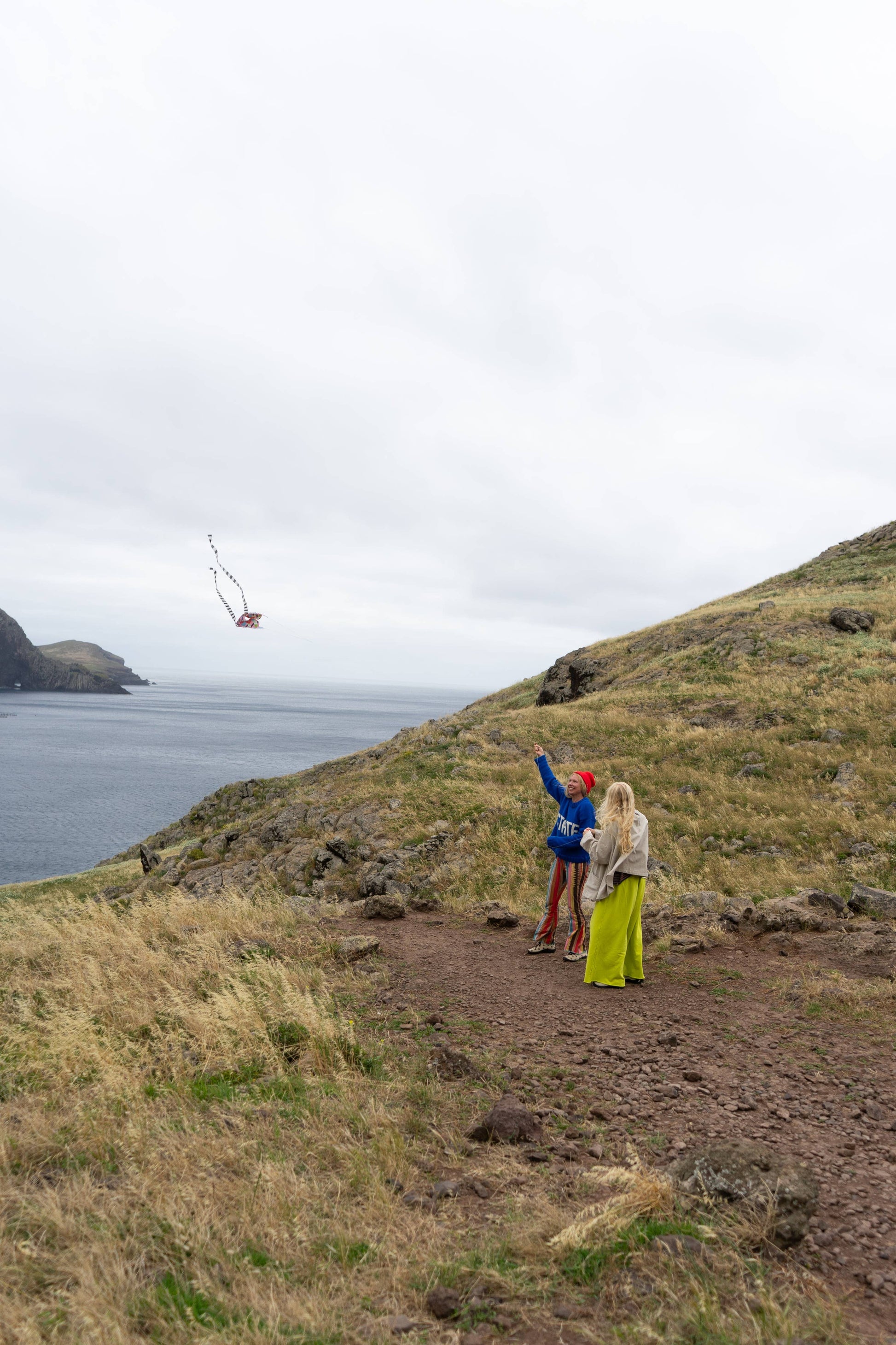 Two people standing on a grassy hill overlooking a body of water with a helicopter in the distance.