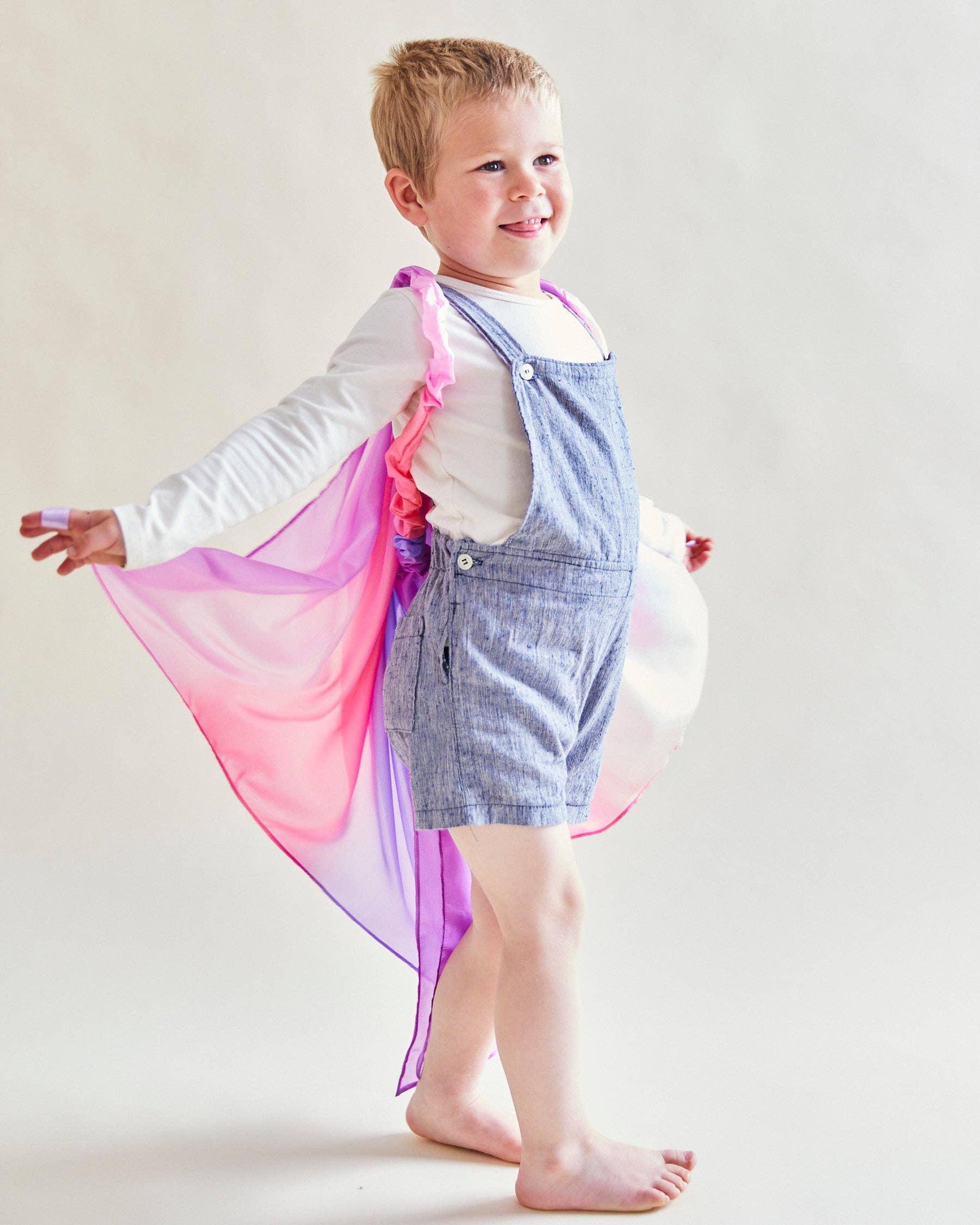 Child wearing a colorful cape and overalls on a plain background