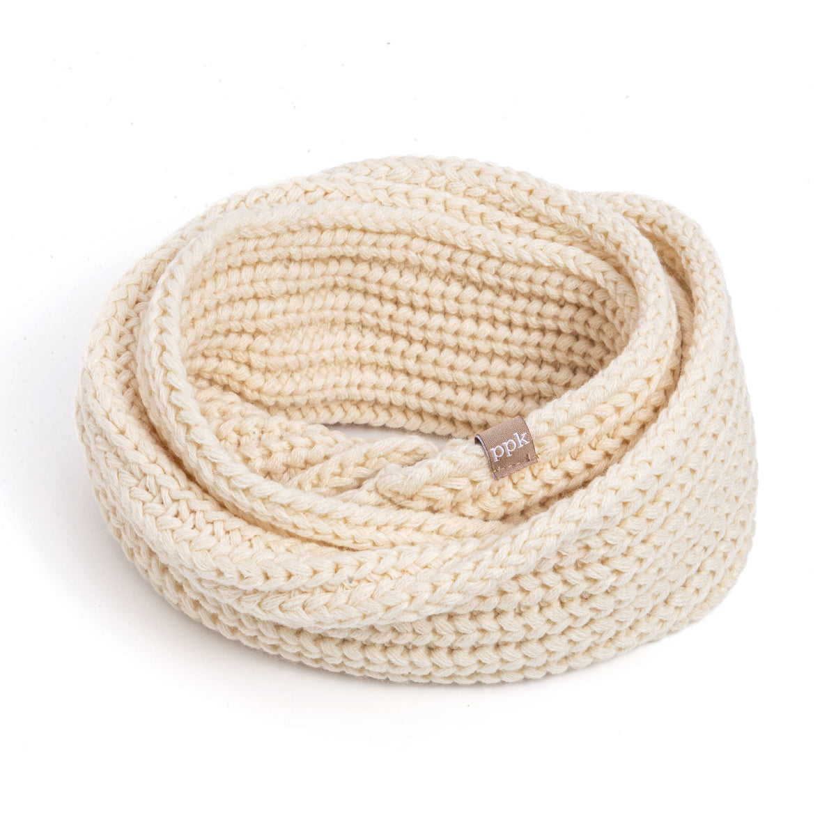 A cream-colored chunky knit infinity scarf coiled on a white background, featuring a small brown brand tag that reads 'pik'.