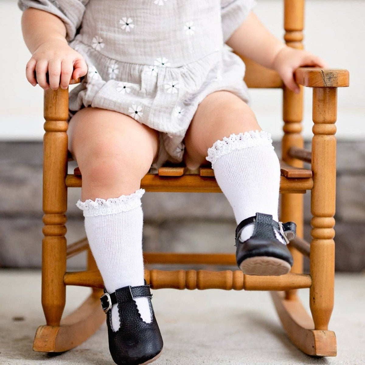 Child sitting on a wooden rocking chair wearing white socks and black shoes.