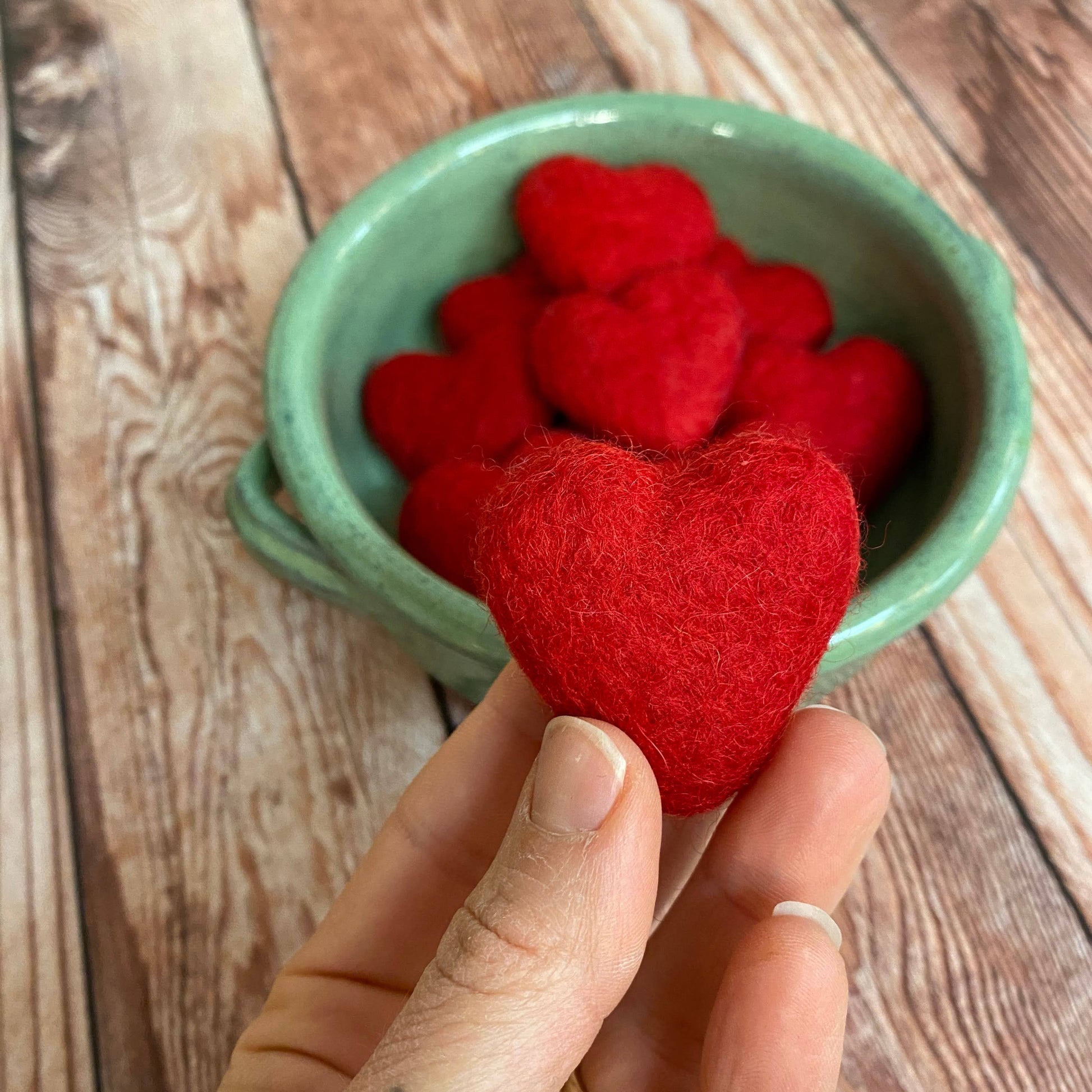 Red heart-shaped objects in a green bowl on a wooden surface