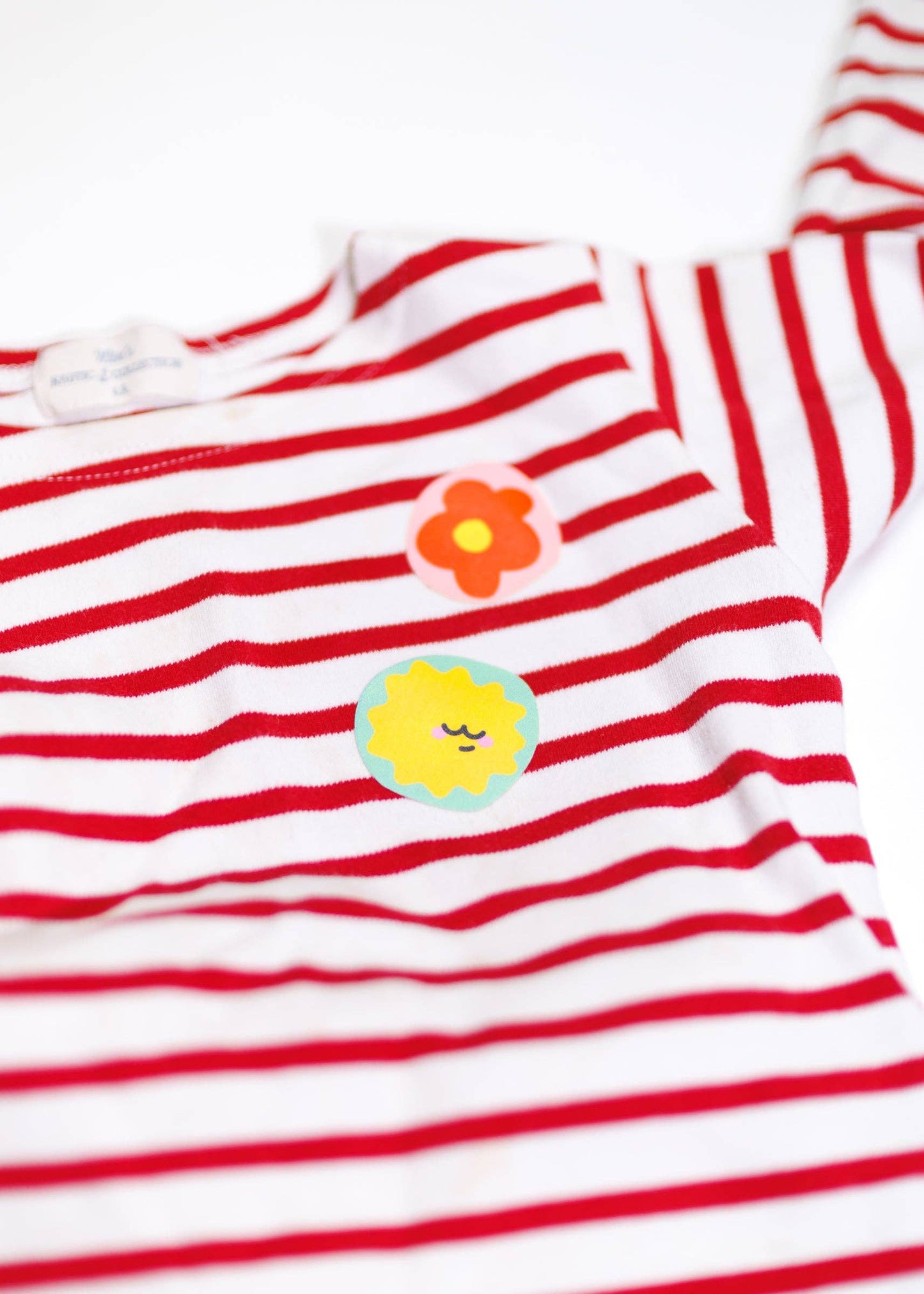 Red and white striped shirt with colorful flower and sun patched on a white background