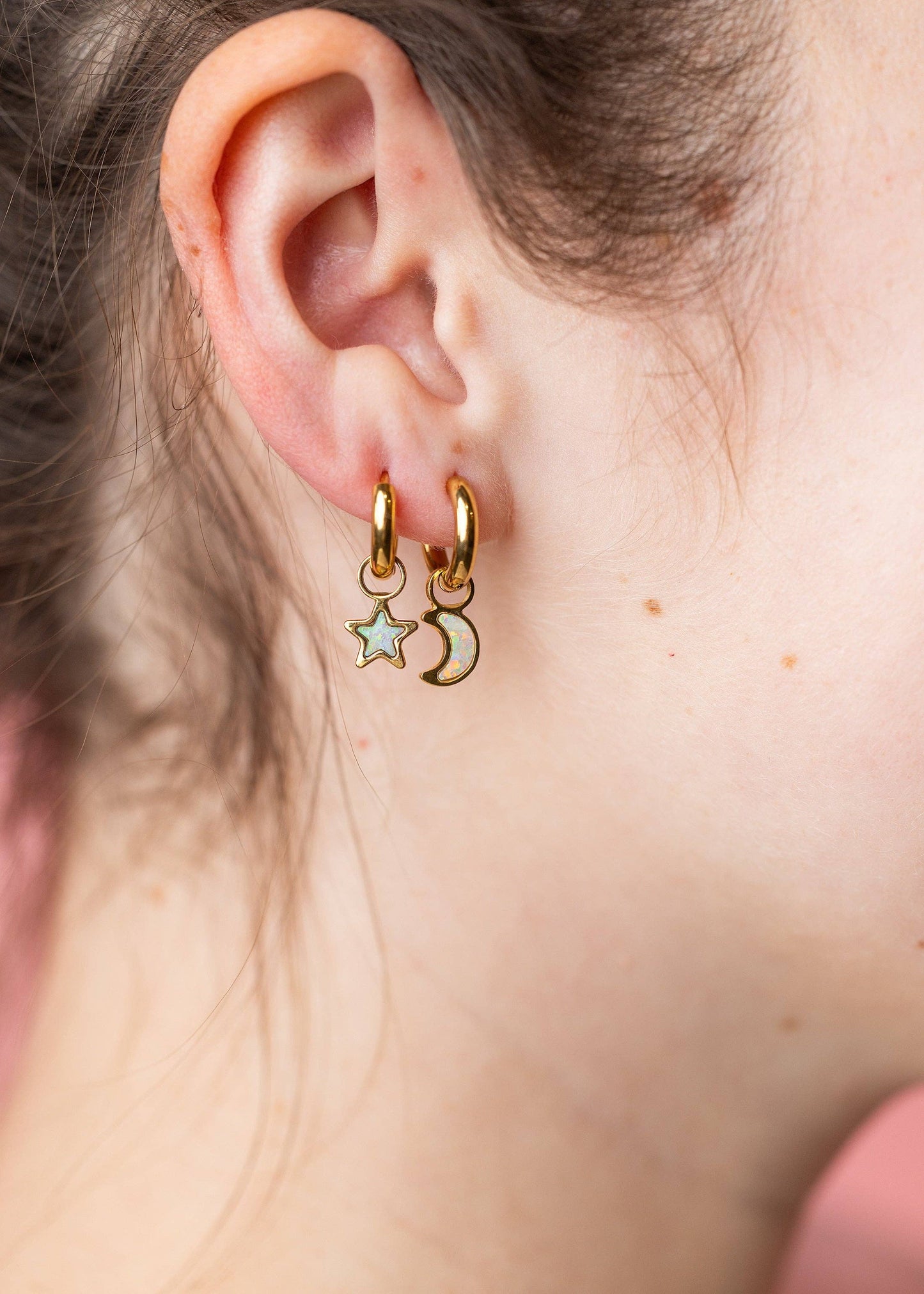 Close-up of an ear wearing gold hoop earrings with star and moon charms.