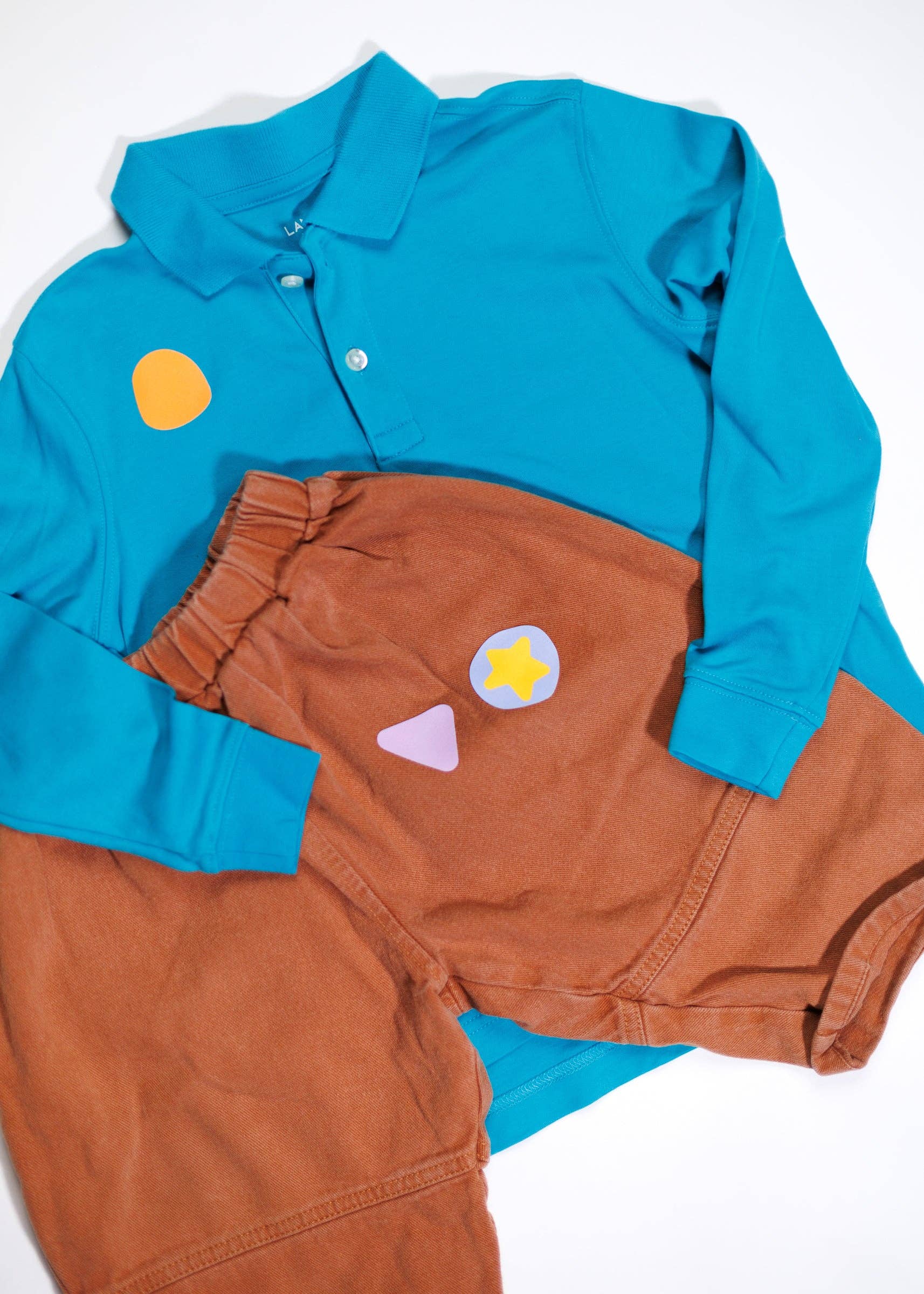 Children's outfit with blue shirt and brown pants featuring colorful patches on a white background
