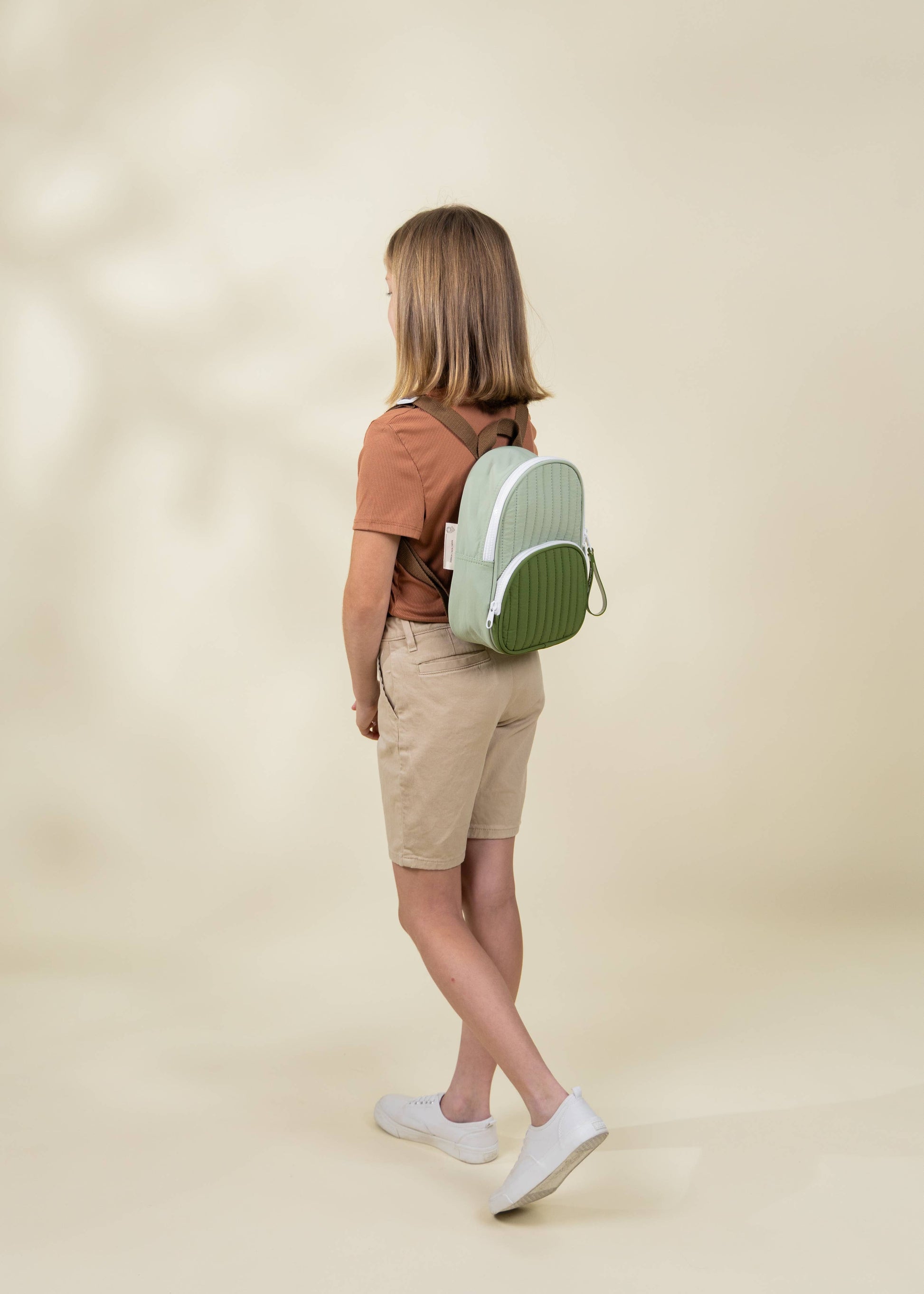 Person wearing a green backpack on a beige background