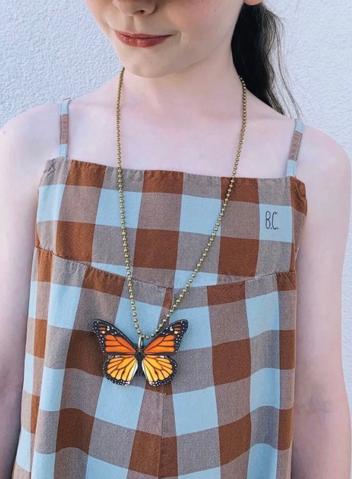 Person wearing a plaid dress with a butterfly pendant necklace against a light background
