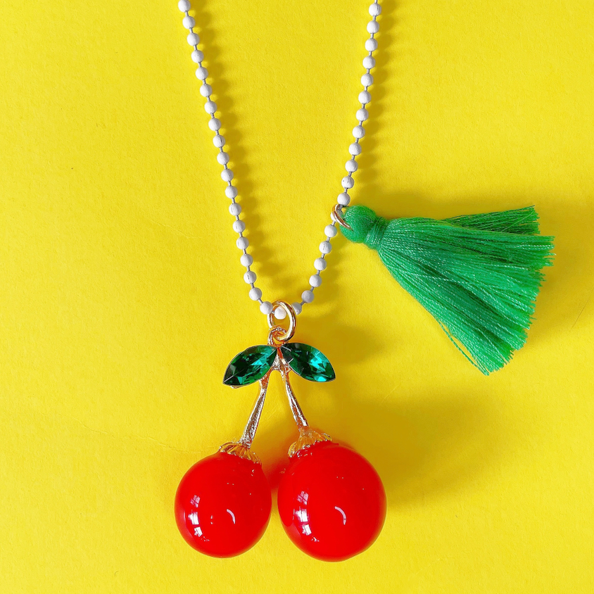 Necklace with red cherry pendants and a green tassel on a yellow background