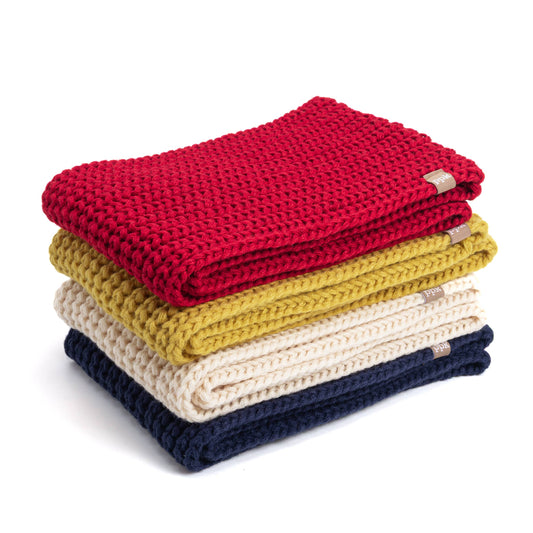 Stack of folded knitted scarves in red, yellow, white, and navy on a white background