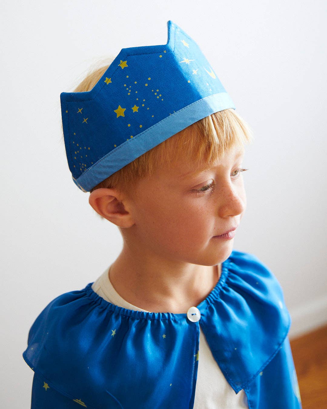 Child wearing a blue star-patterned crown against a white background