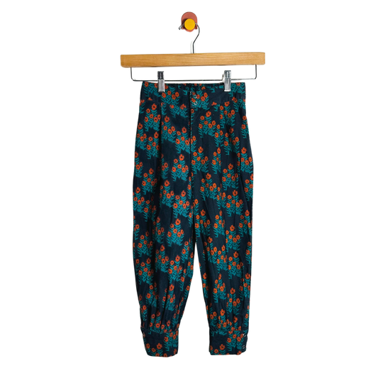 Floral-patterned pants hanging on a wooden hanger against a white background