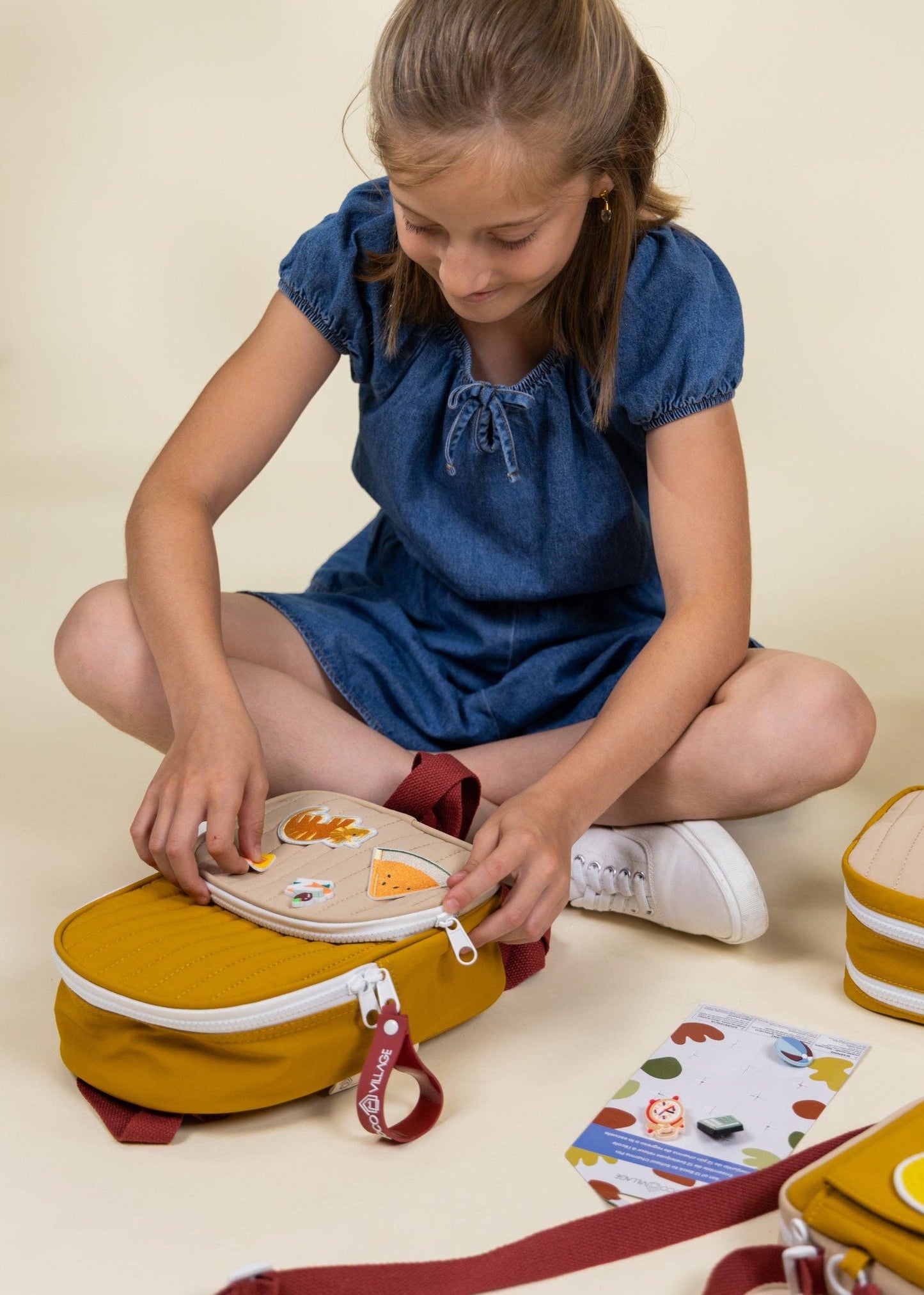 Girl sitting on the floor with a yellow lunch bag and food items, wearing a blue dress.