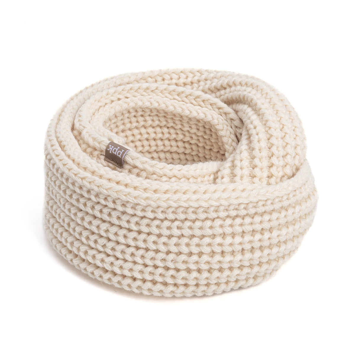 A coiled chunky knit scarf accessory in a warm cream or off-white color, featuring a small woven brand tag. The product is photographed on a seamless white background.
