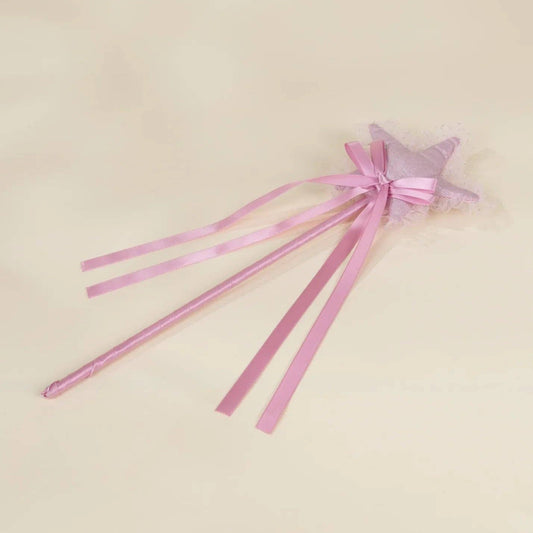 A pink star-shaped wand with long satin ribbons and a small tulle bow, photographed on a plain light beige background.