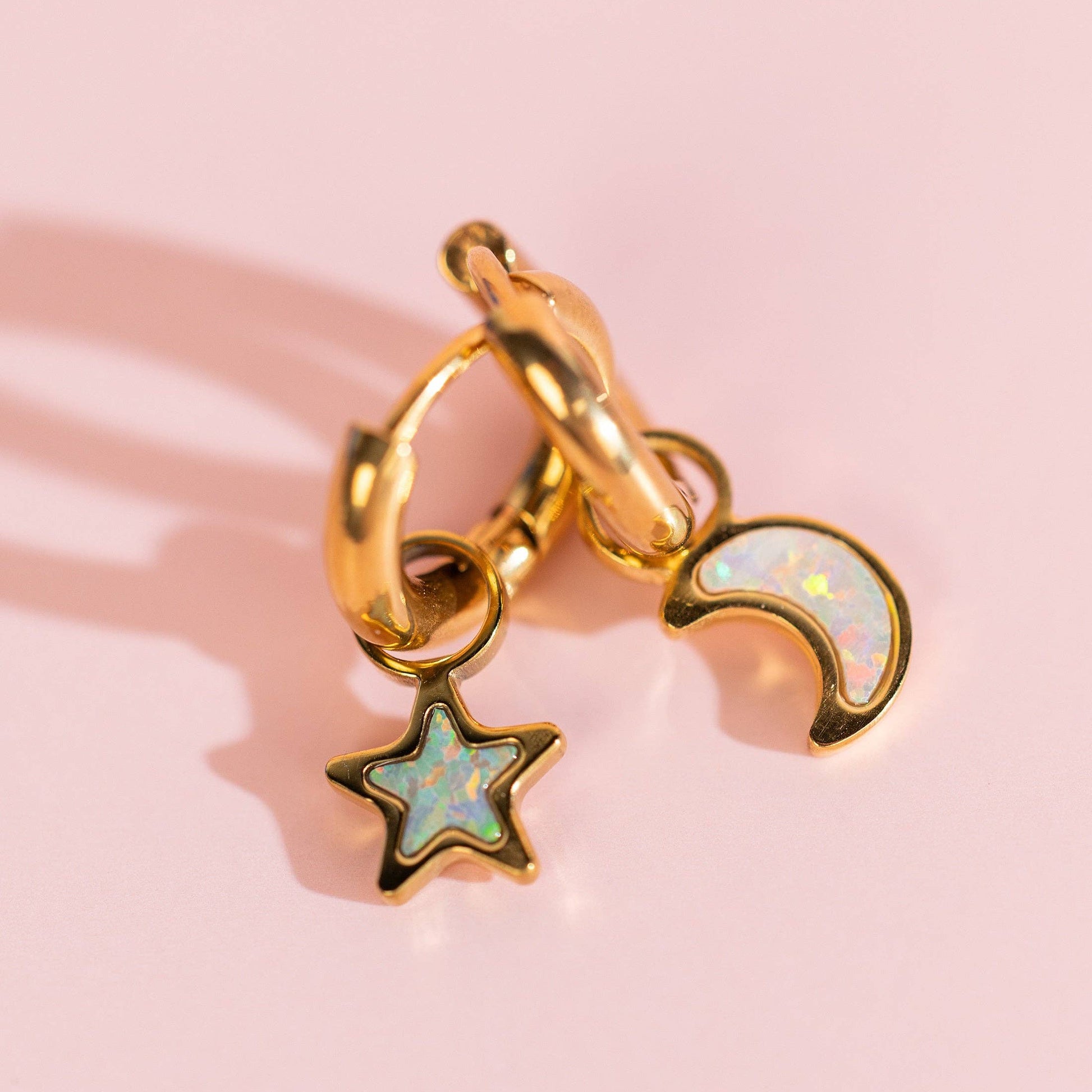 Gold hoop earring with star and moon charms on a pink background