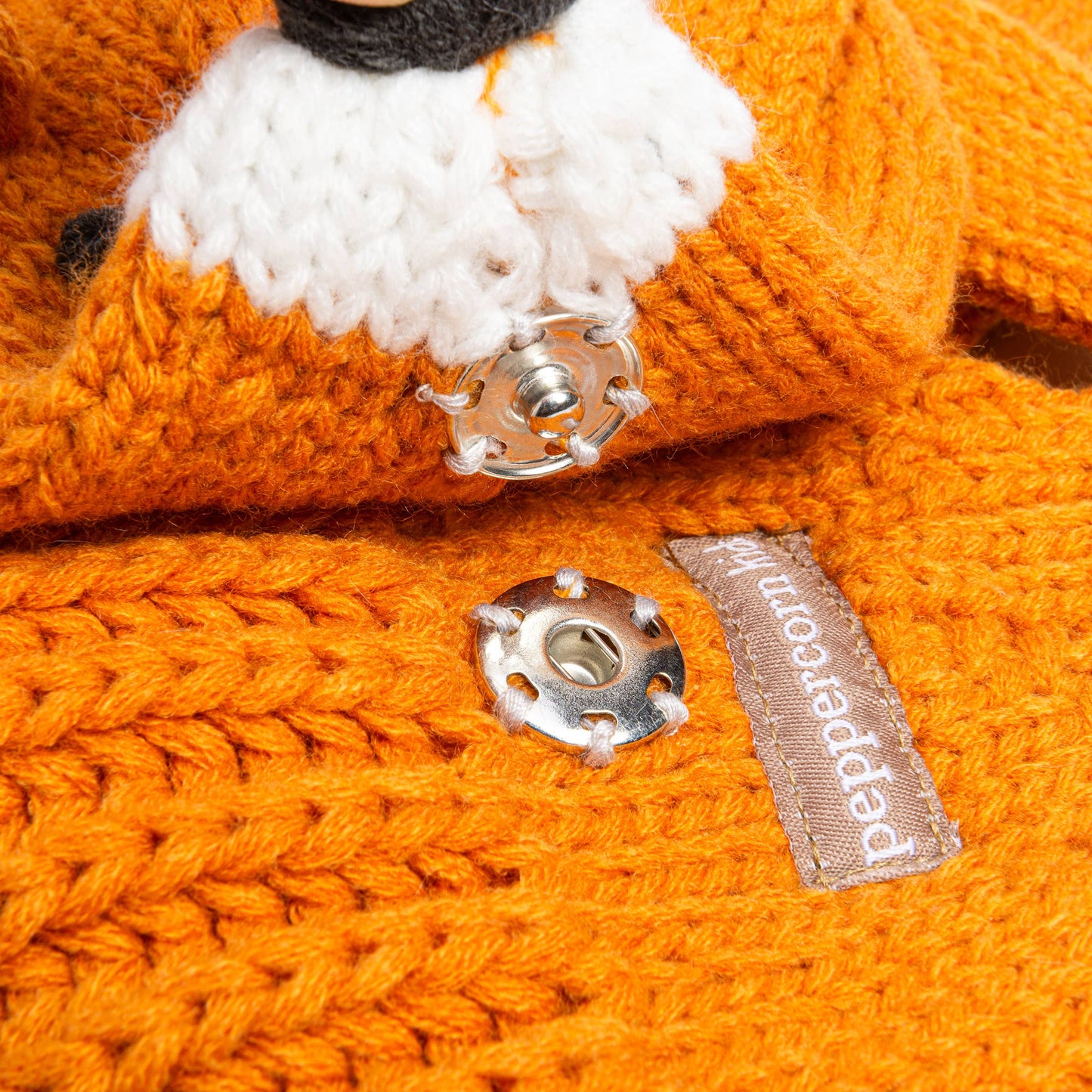 Close-up of an orange knitted item with a button and label, featuring the brand 'Papeterie'.