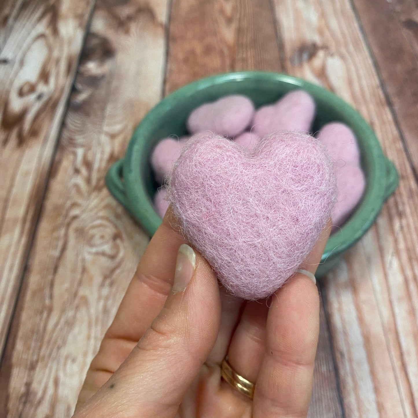 Heart-shaped pink bath bomb held in a hand with a wooden background