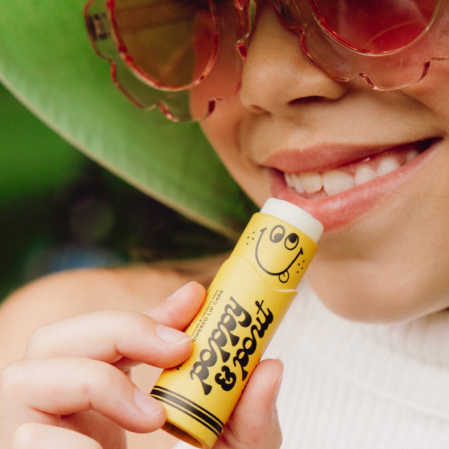 Person holding a yellow lip balm with a smiley face design outdoors