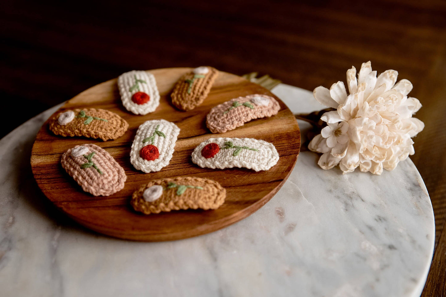 Wooden board with crocheted hair clips on a marble surface with a white flower.