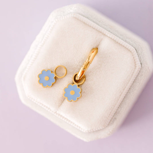 Gold and blue flower-shaped earrings on a white jewelry box with a light purple background