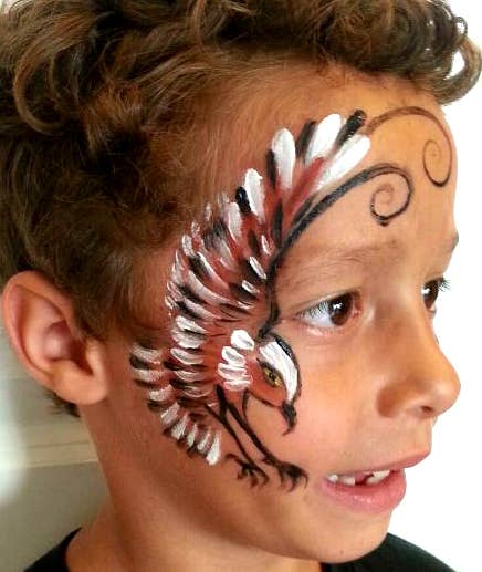 Child with face paint resembling a dragon on a plain background